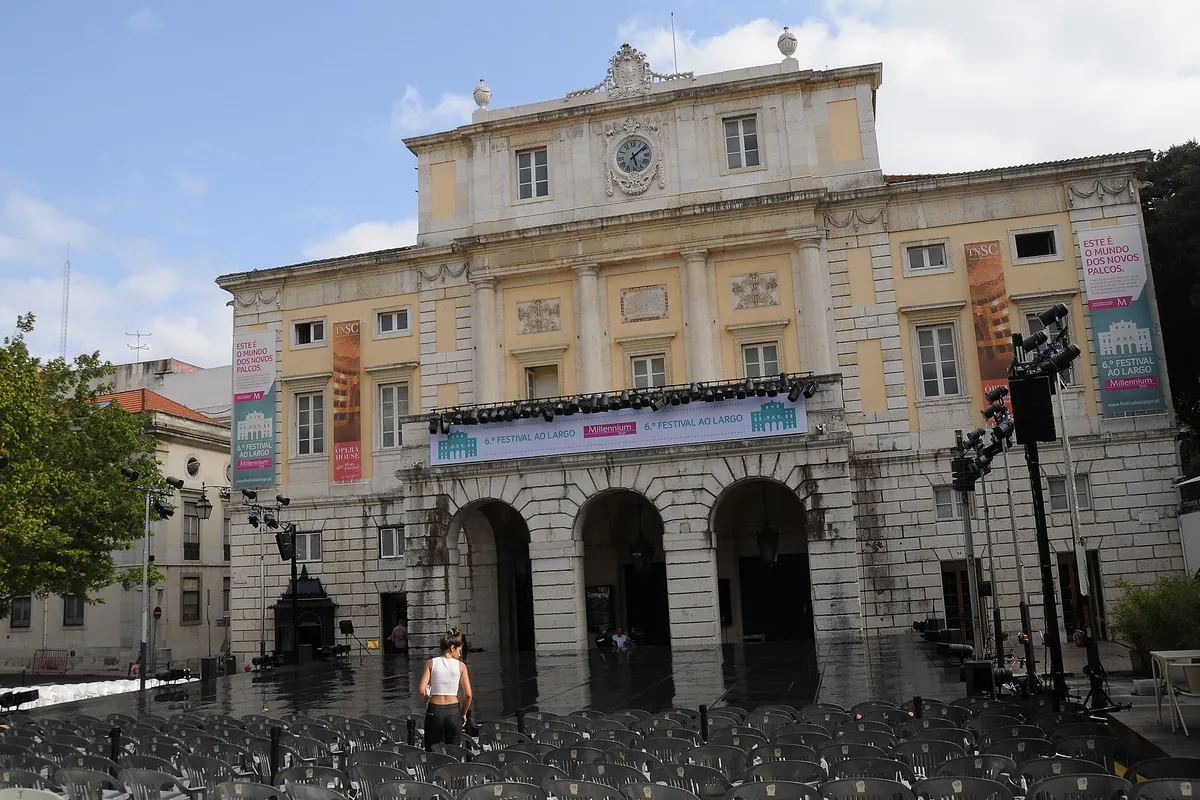 Bladożółta neoklasyczna fasada Teatro Nacional de São Carlos z trzema arkadami na poziomie ulicy.